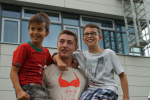Ein älterer Schüler mit zwei jüngeren Schülern auf dem Arm