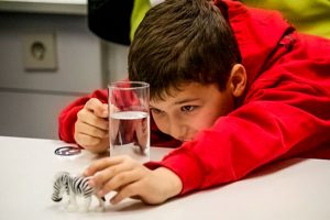 Schüler betrachtet eine Zebra-Figur durch ein Wasserglas